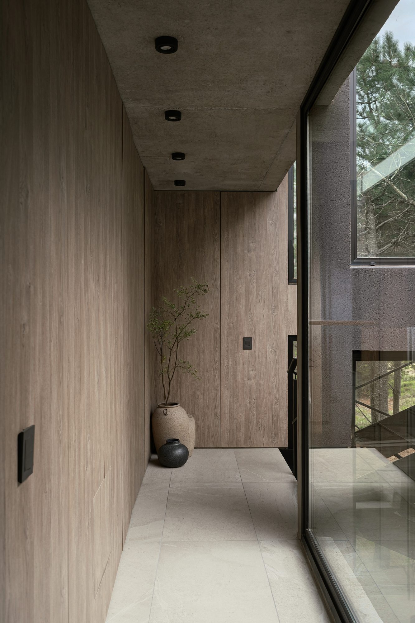 Pasillo interior con muro de madera y hormigón visto, ventanal al bosque — CORNER Arquitectura