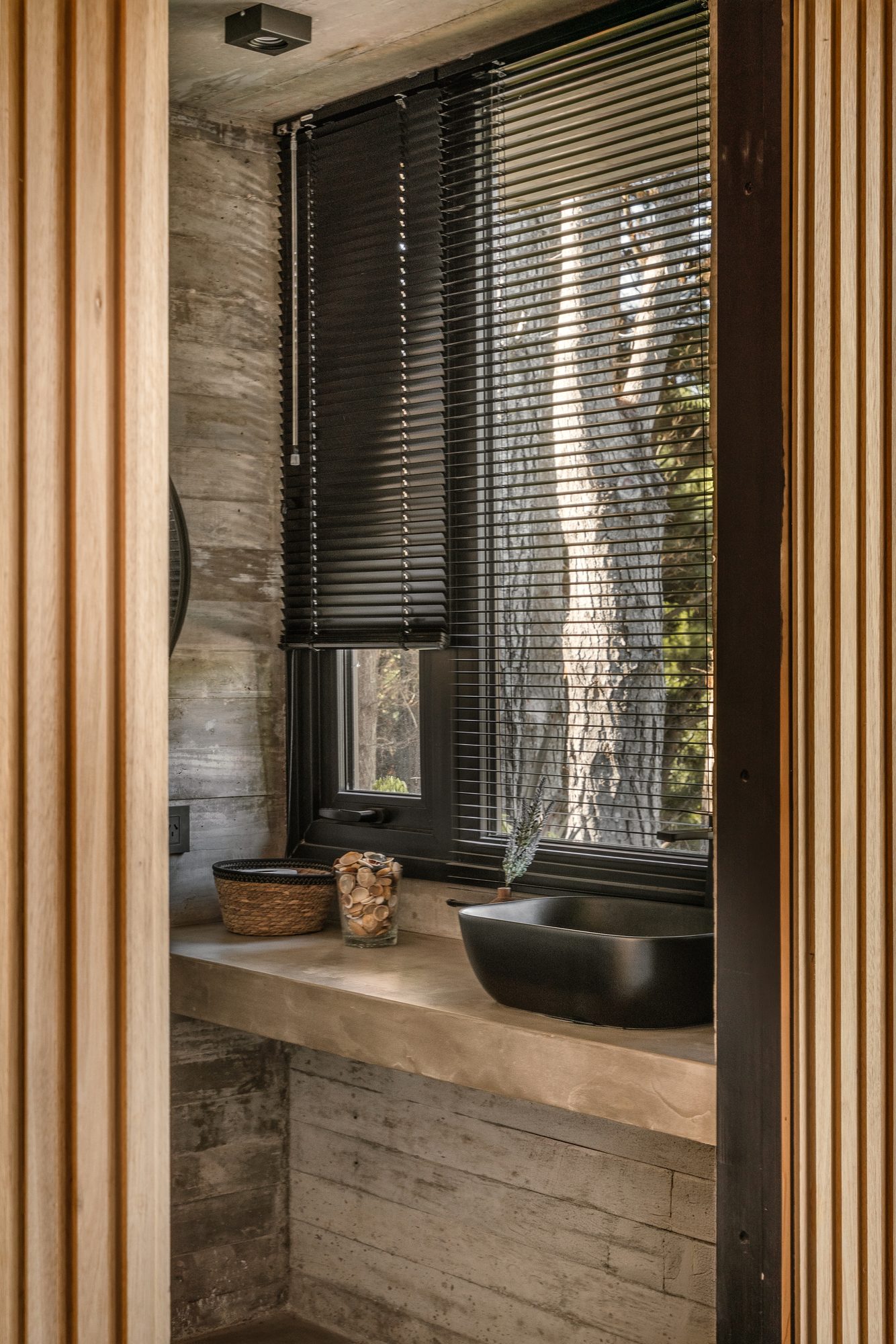 Baño con mesada de hormigón, bacha negra y postigo de madera — CORNER Arquitectura