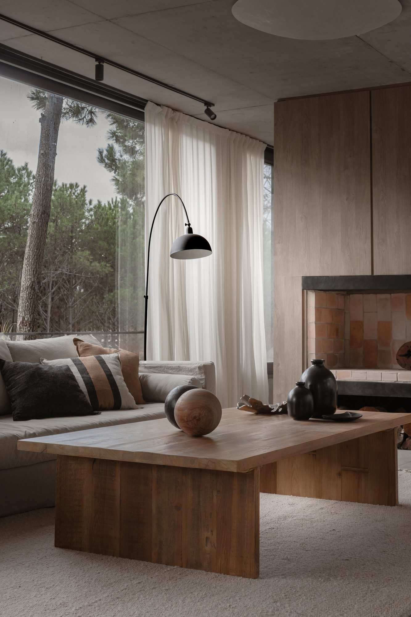 Living con lámpara de pie y mesa baja de madera, ventanal al pinar — CORNER Arquitectura
