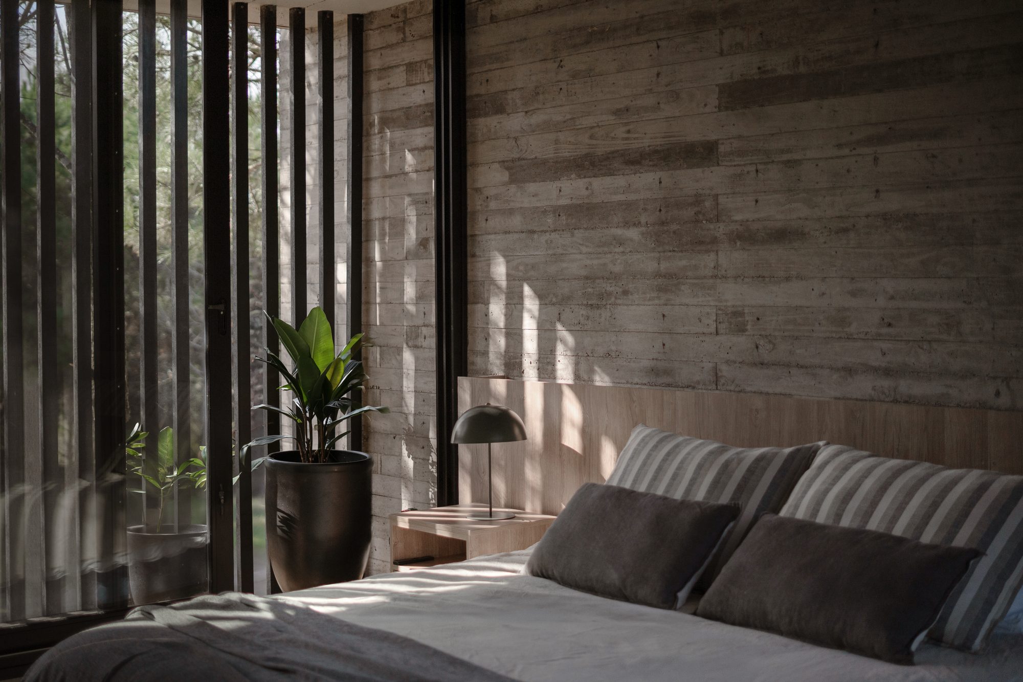 Dormitorio con cabecera de madera y plantas, con celosía filtrando el sol — CORNER Arquitectura