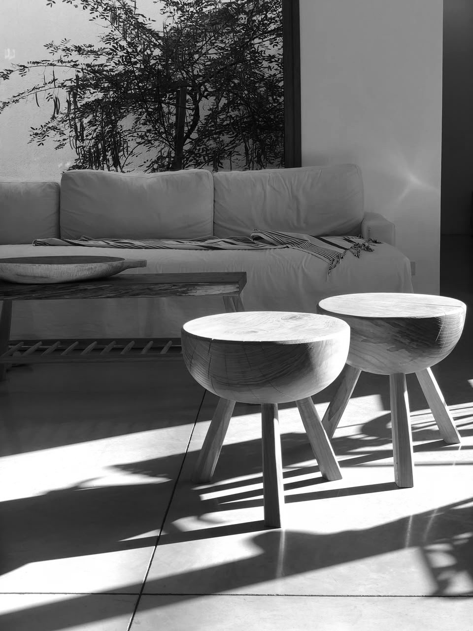 Banquetas de madera y sofá con la luz de la tarde, en blanco y negro — CORNER Arquitectura