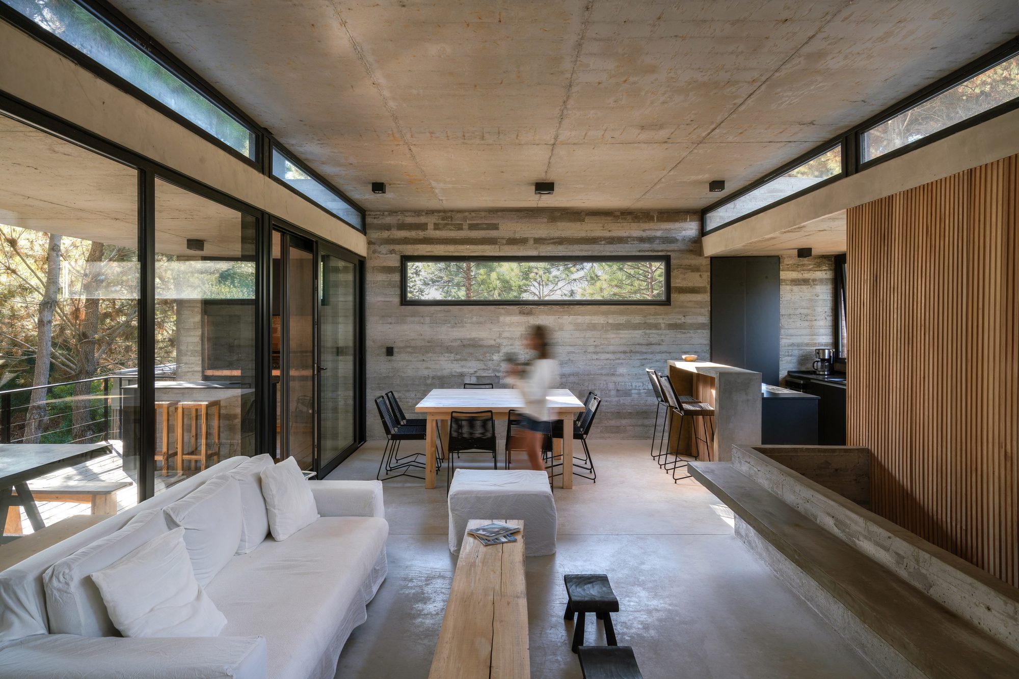 Living, comedor y cocina integrados bajo losa de hormigón, con ventanales al bosque — CORNER Arquitectura