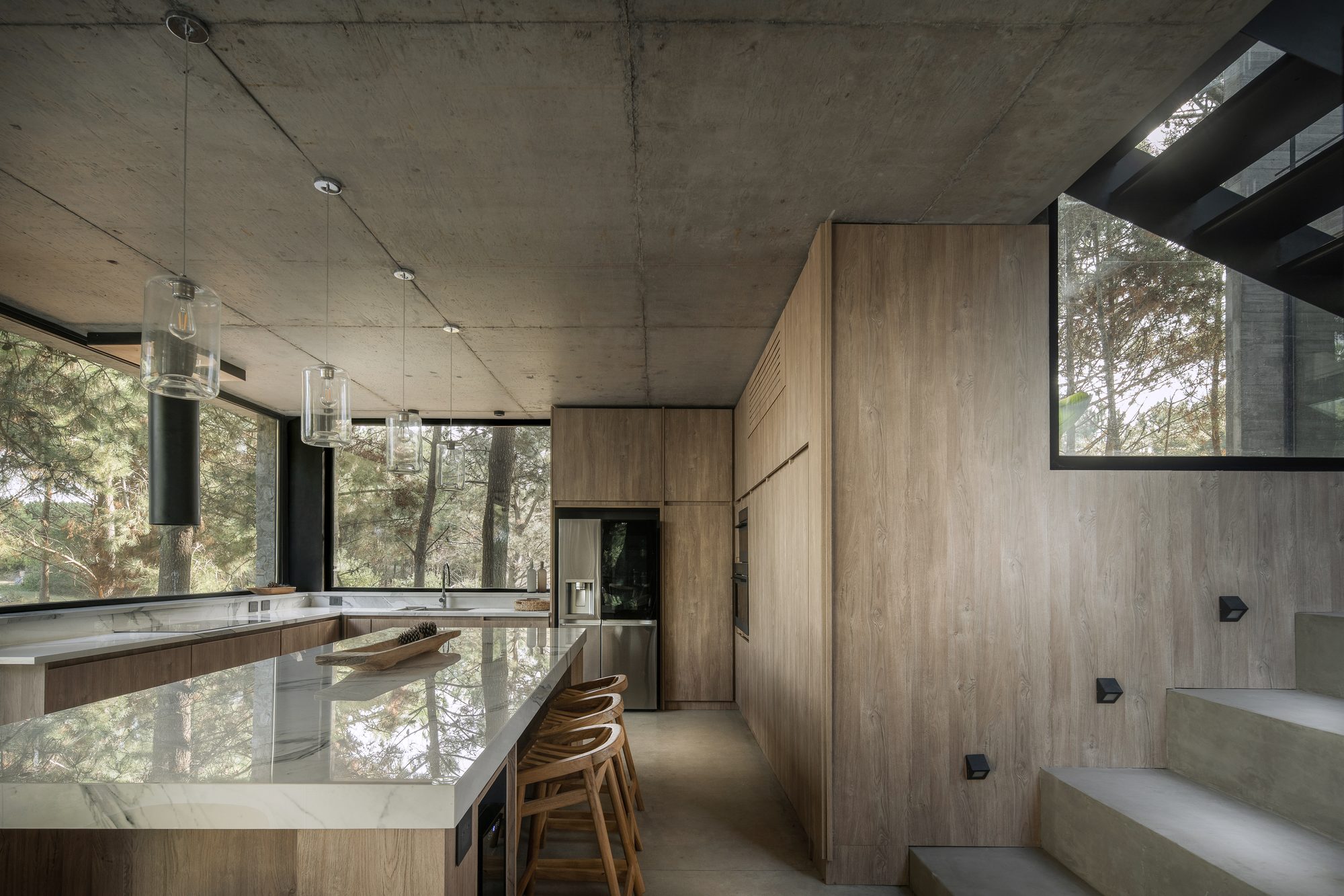 Cocina con isla de mármol, artefactos colgantes y escalera de hormigón — CORNER Arquitectura