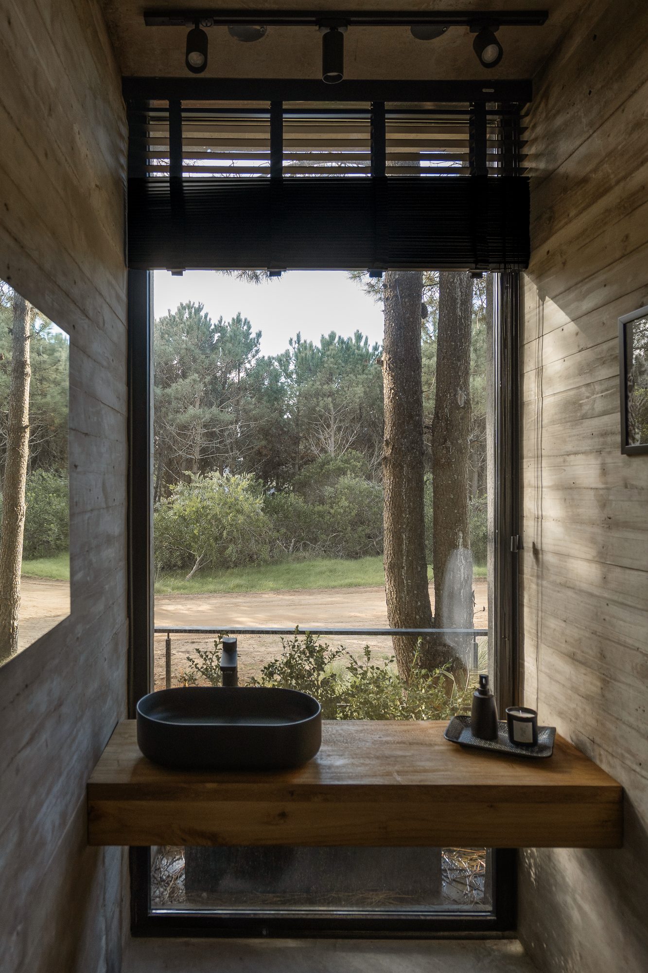 Baño con bacha negra sobre mesada de madera y ventana al pinar — CORNER Arquitectura