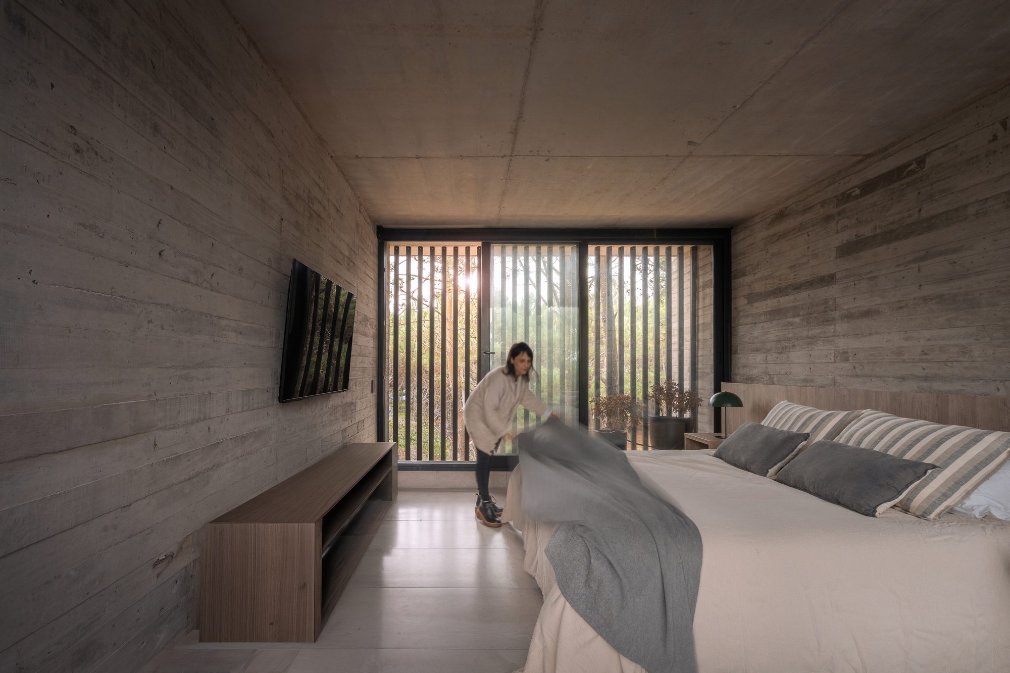 Dormitorio amplio de hormigón visto con mueble bajo y celosía al fondo — CORNER Arquitectura