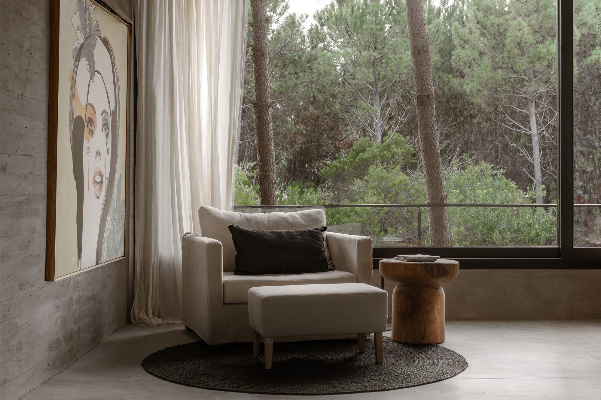 Rincón de lectura con sillón, alfombra redonda y ventanal al pinar — CORNER Arquitectura