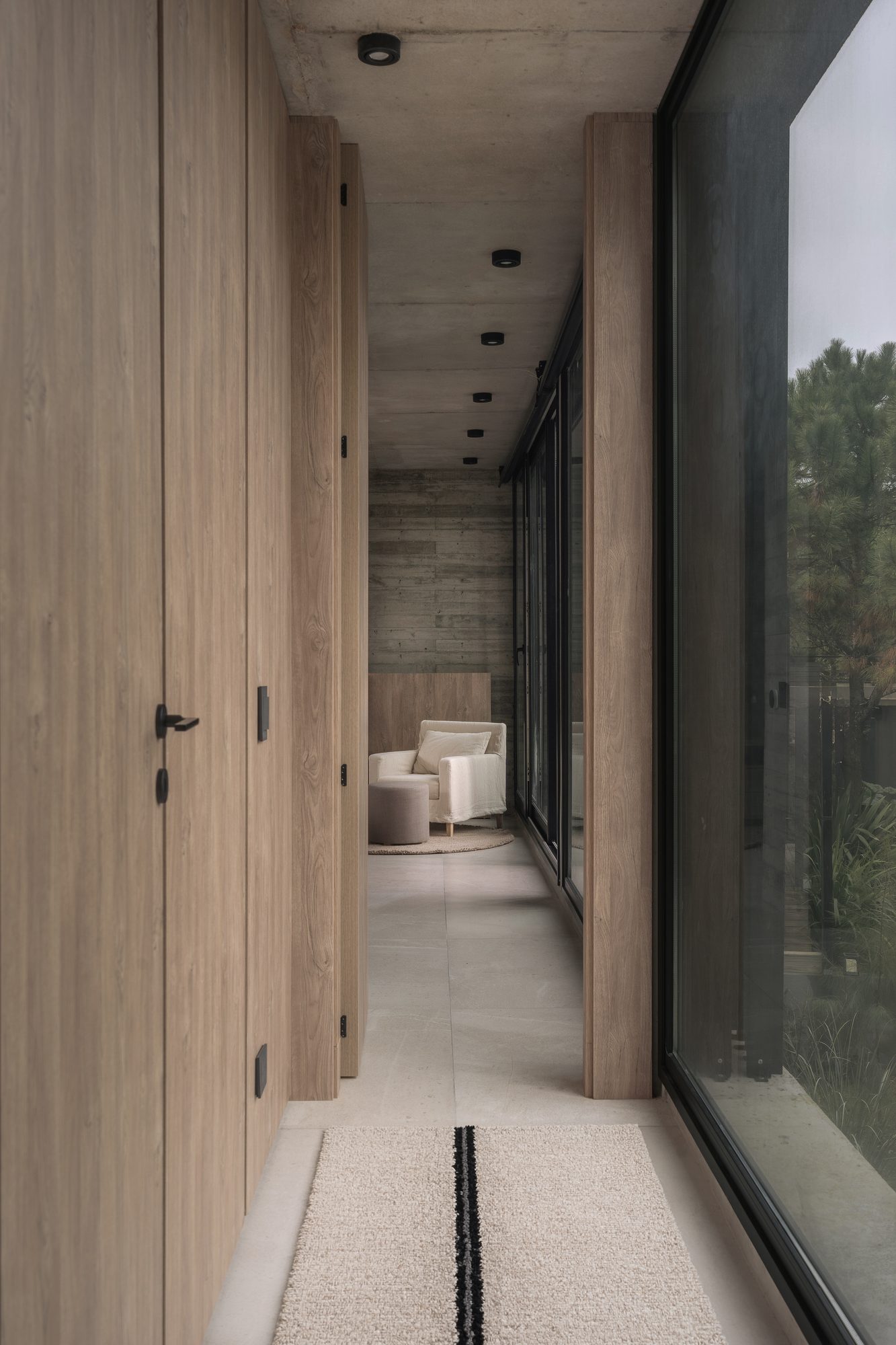 Circulación interior con puertas de madera y ventanal lateral corrido — CORNER Arquitectura