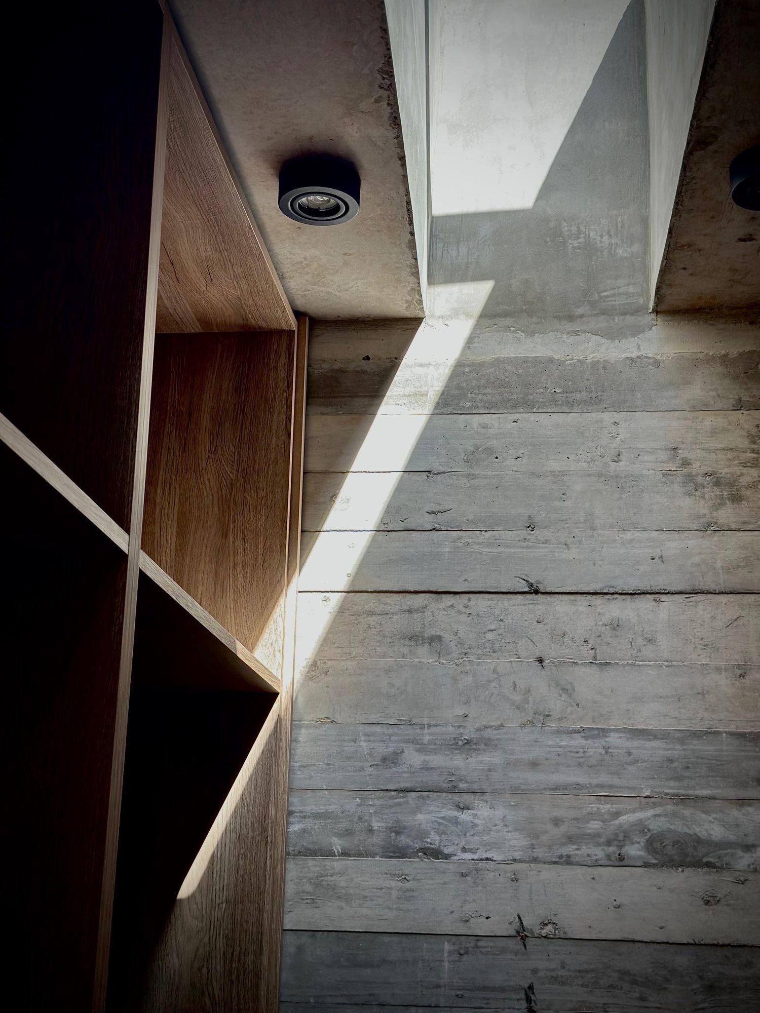 Detalle del encuentro entre un mueble de madera y el muro de hormigón, con luz rasante — CORNER Arquitectura