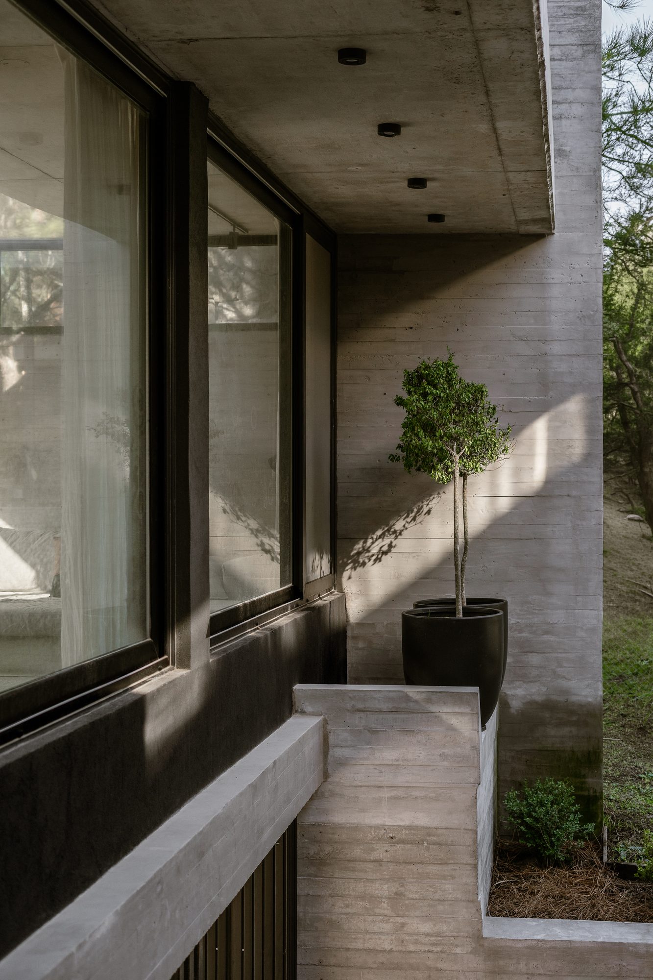 Galería exterior con banco de hormigón, macetas y ventanales — CORNER Arquitectura