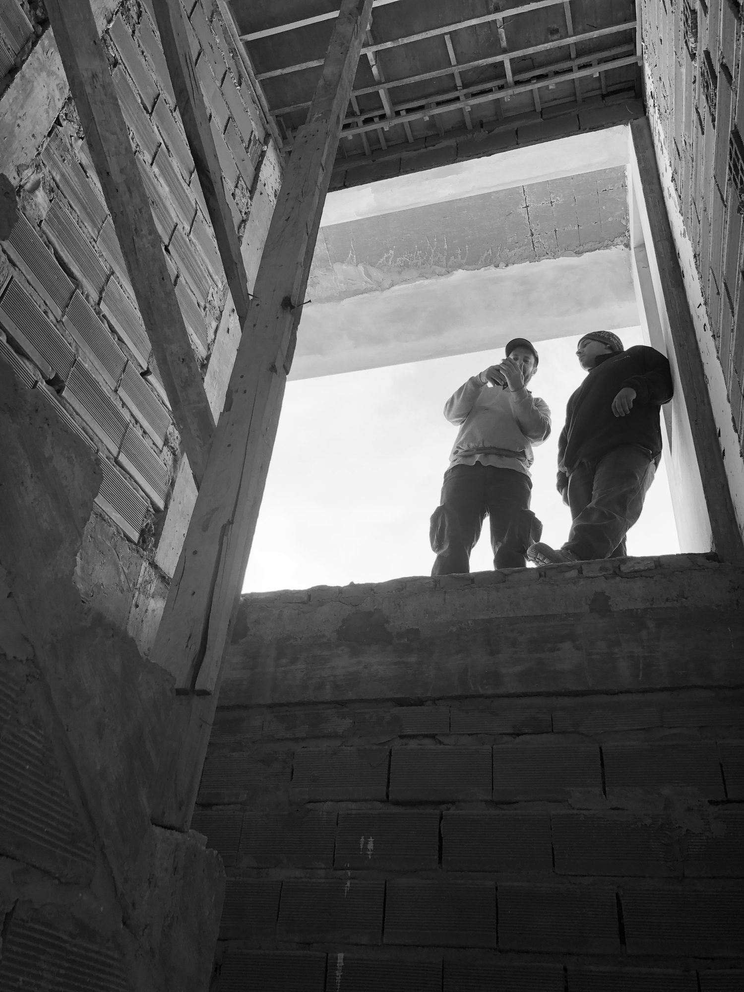 Contrapicado desde el subsuelo de una obra, con dos personas asomadas al borde de la losa — CORNER Arquitectura